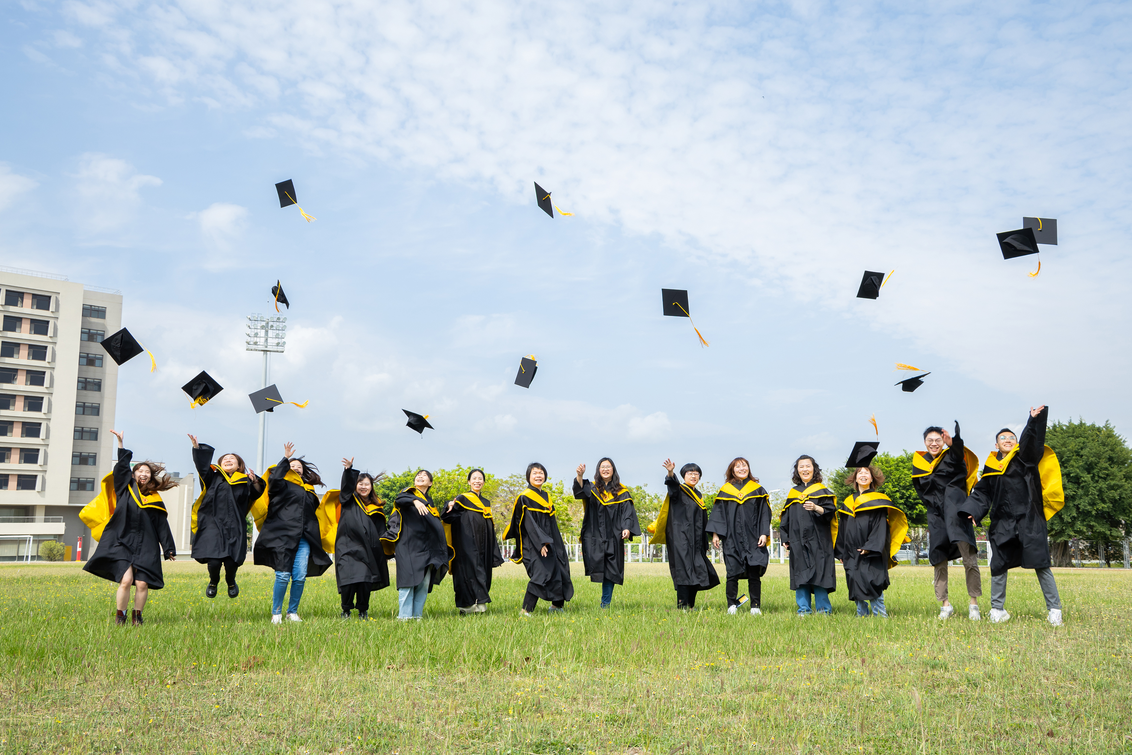 本系研究所畢業生於草地上拋學士帽慶祝畢業合影